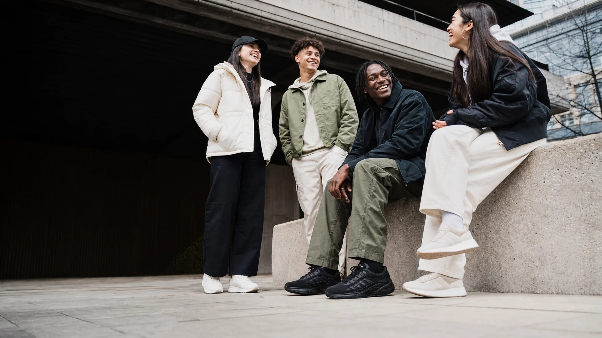 A group of friends in casual trainers laughing together on a city ledge.
